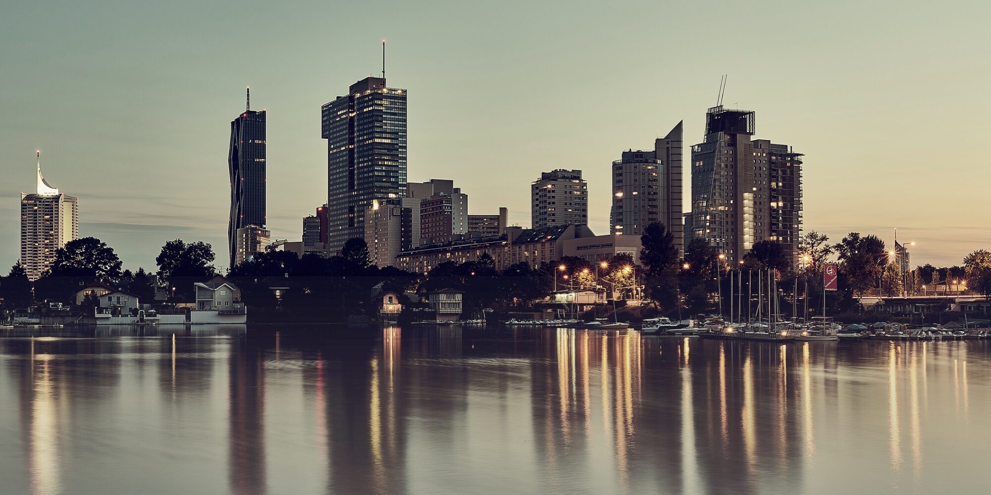 Stadtskyline in der Abenddämmerung mit beleuchteten Hochhäusern, die sich im ruhigen Wasser eines Flusses oder Hafenbeckens spiegeln